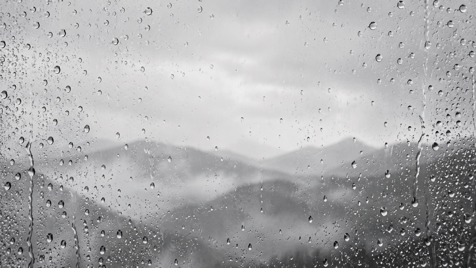 Delicate raindrops and flowing rivulets on glass, with a soft mountain landscape beyond